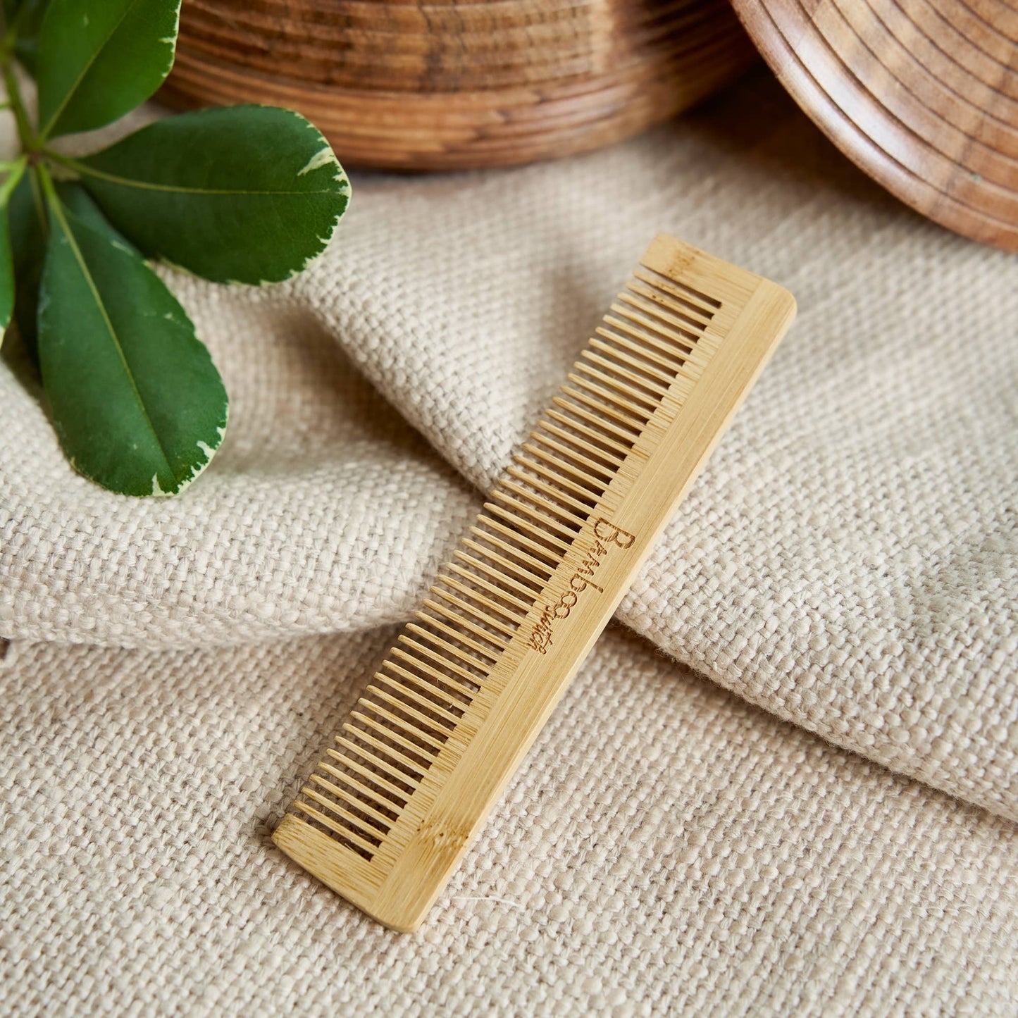 Bamboo comb on a textured fabric surface with a plant leaf in the corner