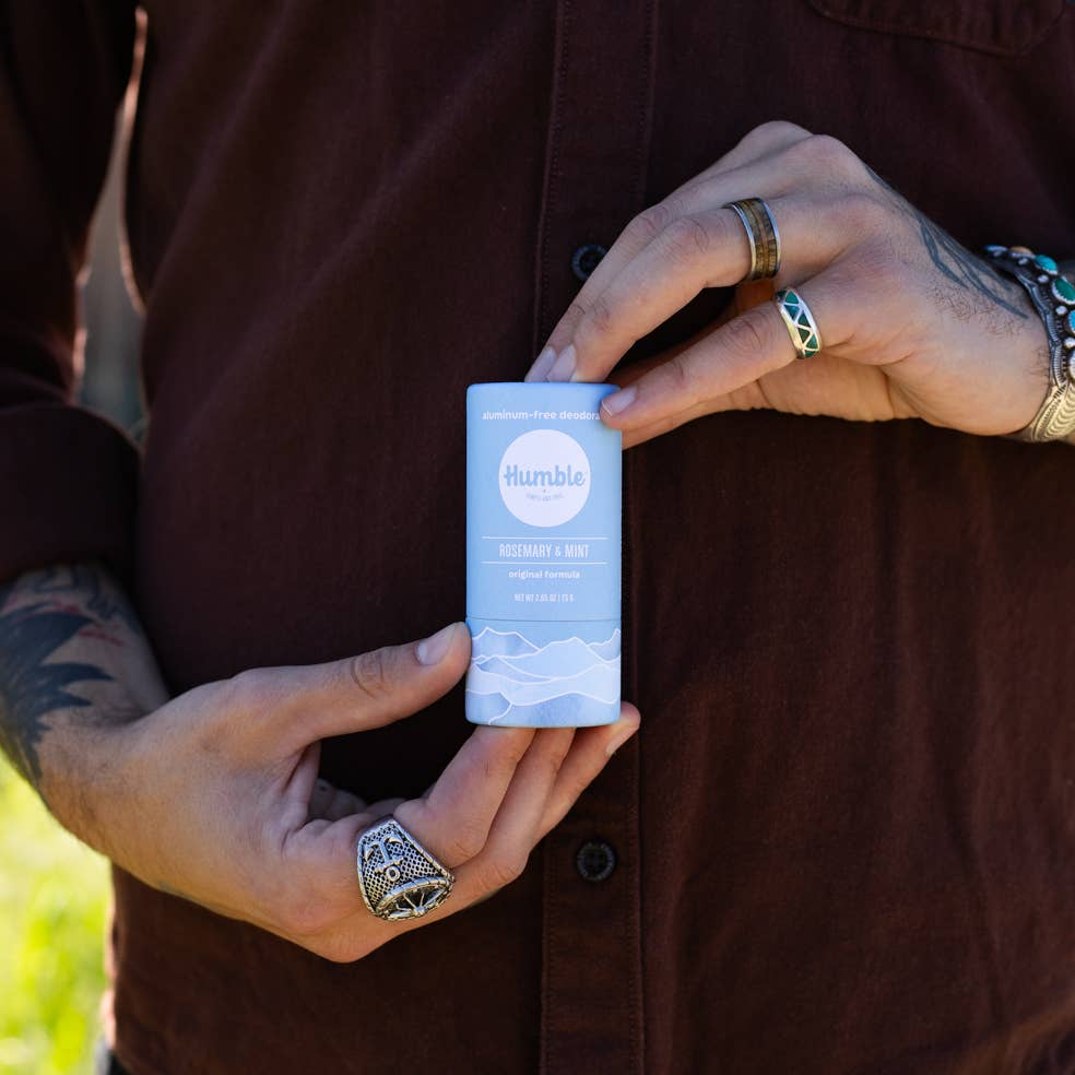 Person holding a blue container labeled 'Humble' with a scenic design, outdoors.