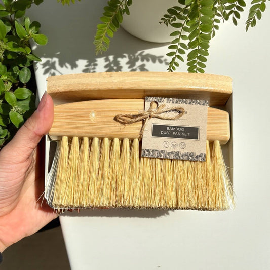 Bamboo dust pan set with a label held by a hand, against a light background with greenery.