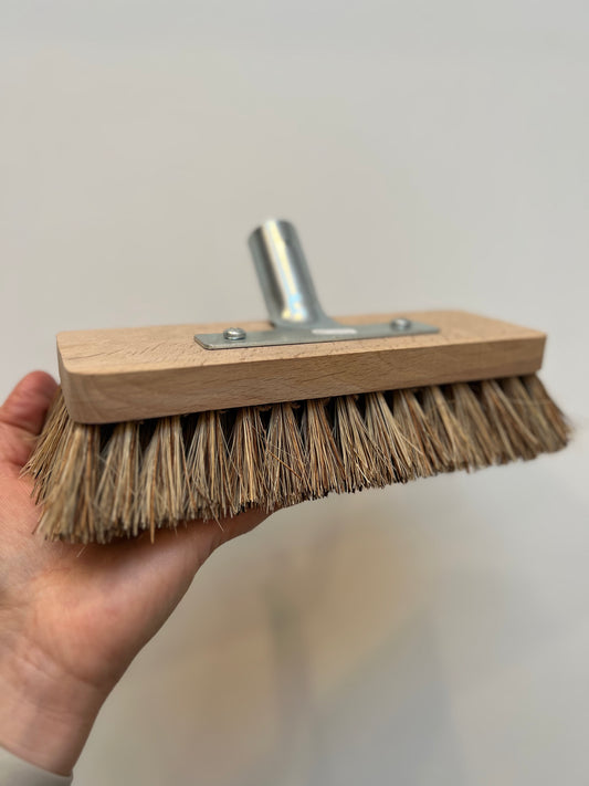 A scrub brush with stiff bristles attached to a wooden base with a metal plate, handle not included.