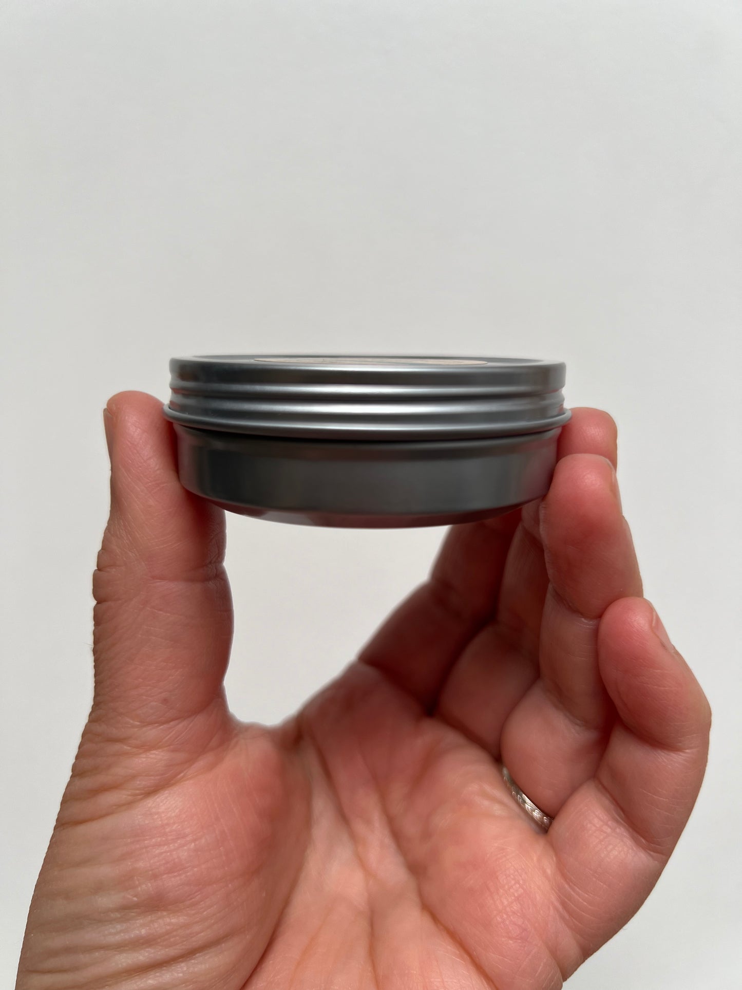 hand holding metal tin showing side of tin with metal twist lid closure