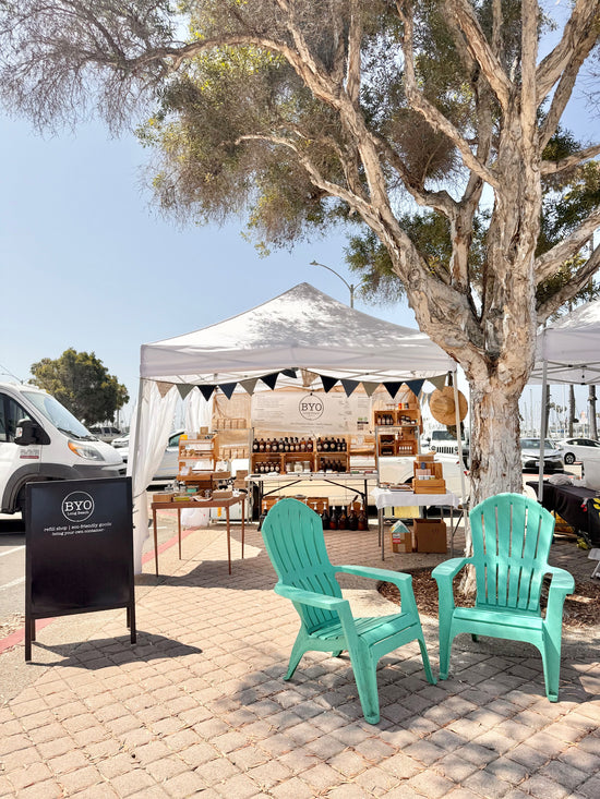 Outdoor market stall with green chairs and BYO branding under a tree.