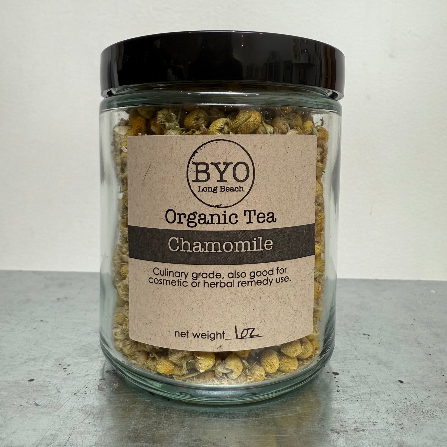 Glass jar of chamomile tea with a brown label on a gray surface.