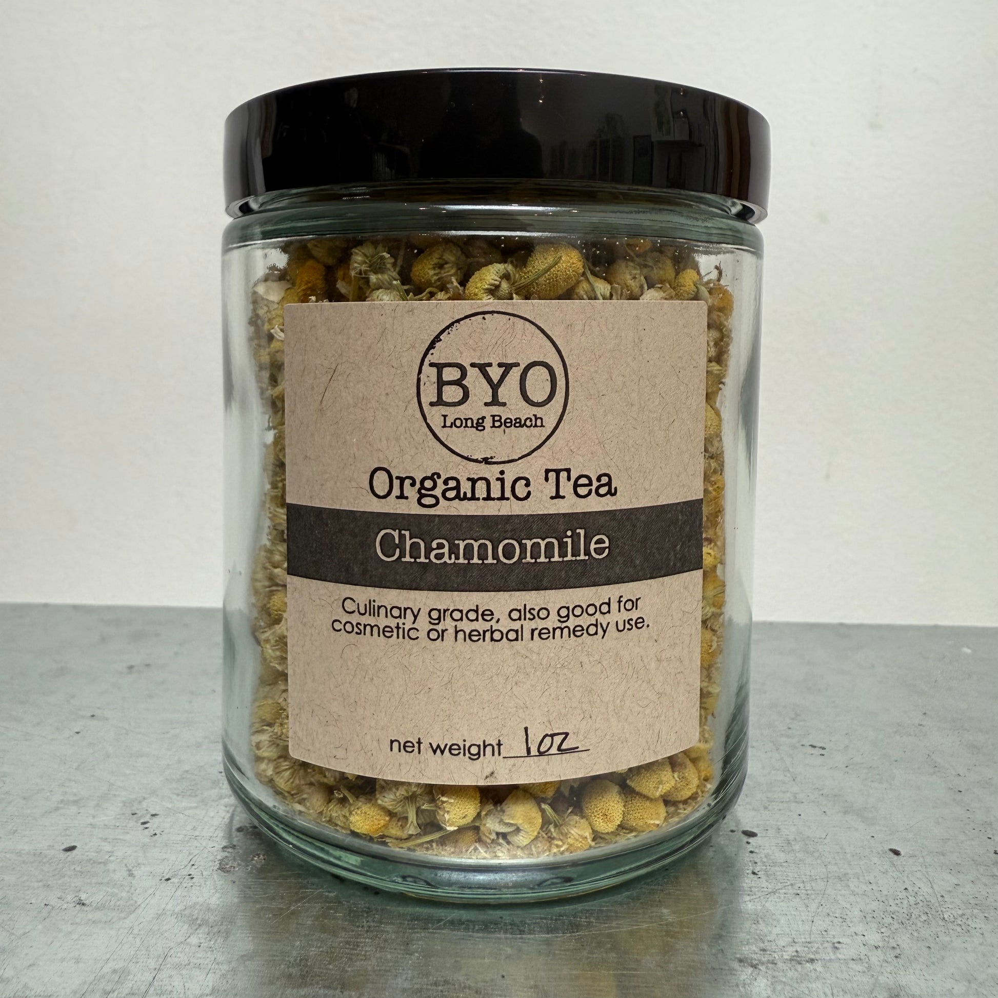 Glass jar of chamomile tea with a brown label on a gray surface.