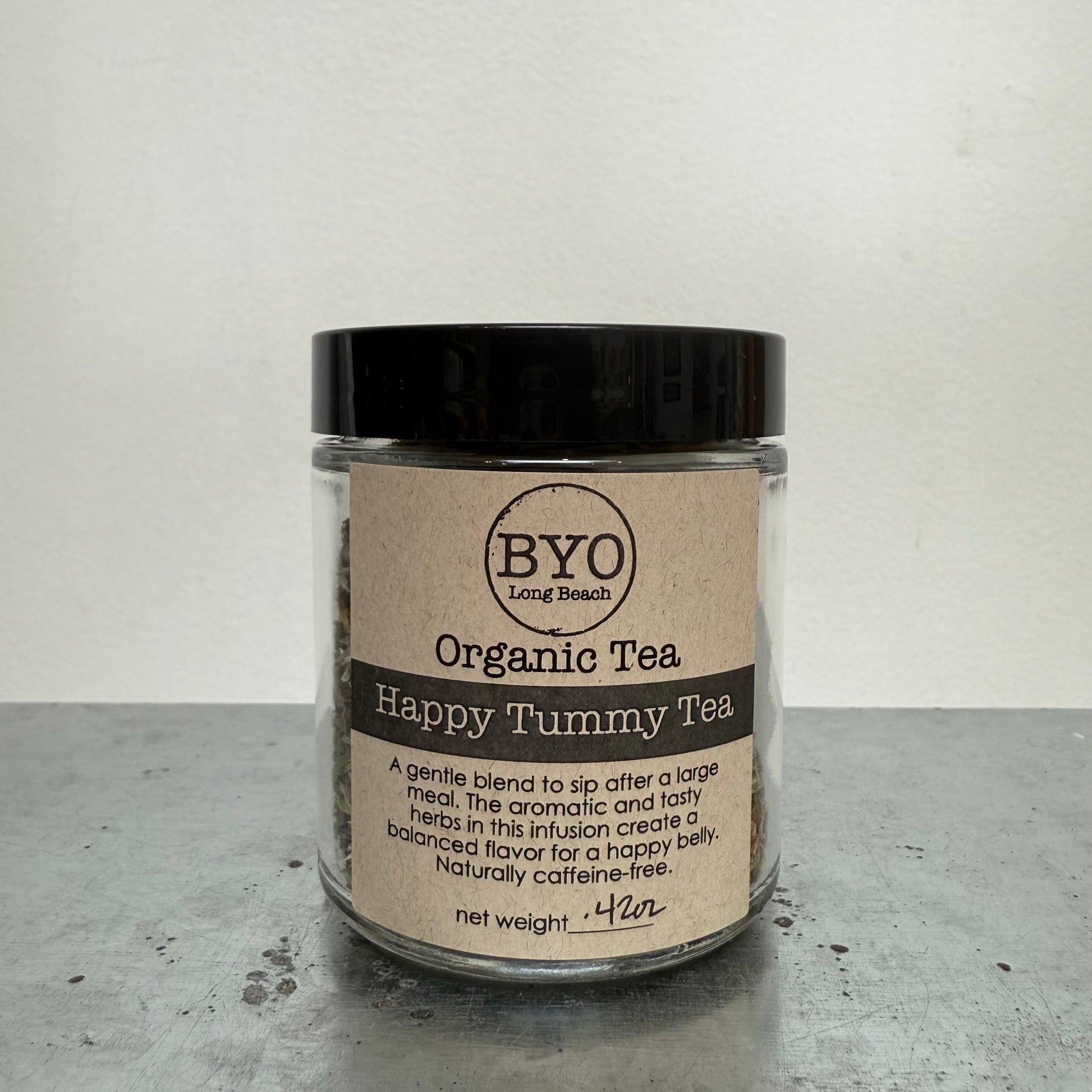 Jar of Organic Tea labeled 'Happy Tummy Tea' by BYO on a gray surface with a white background