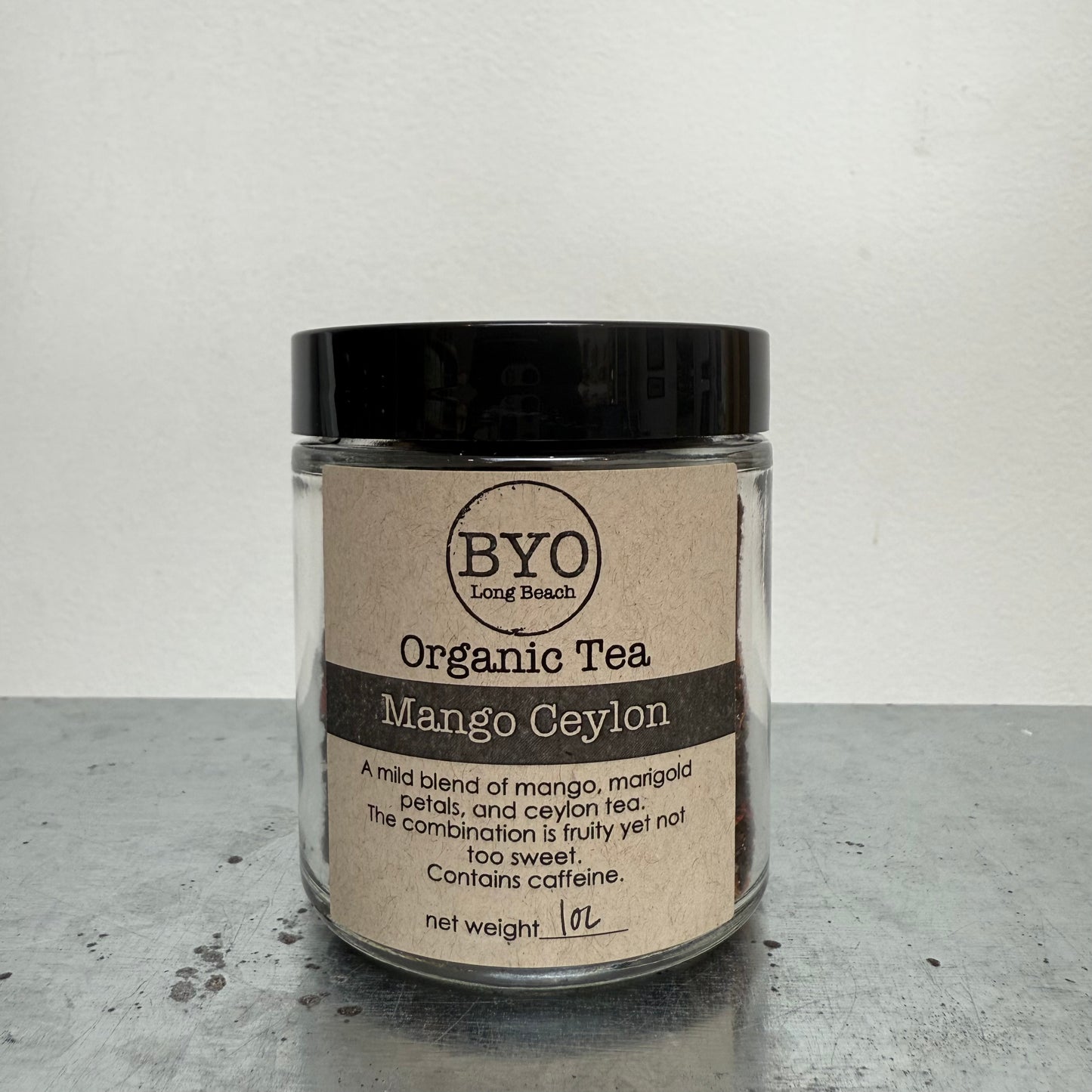 Glass jar of Organic Tea Mango Ceylon with a black lid on a gray surface.