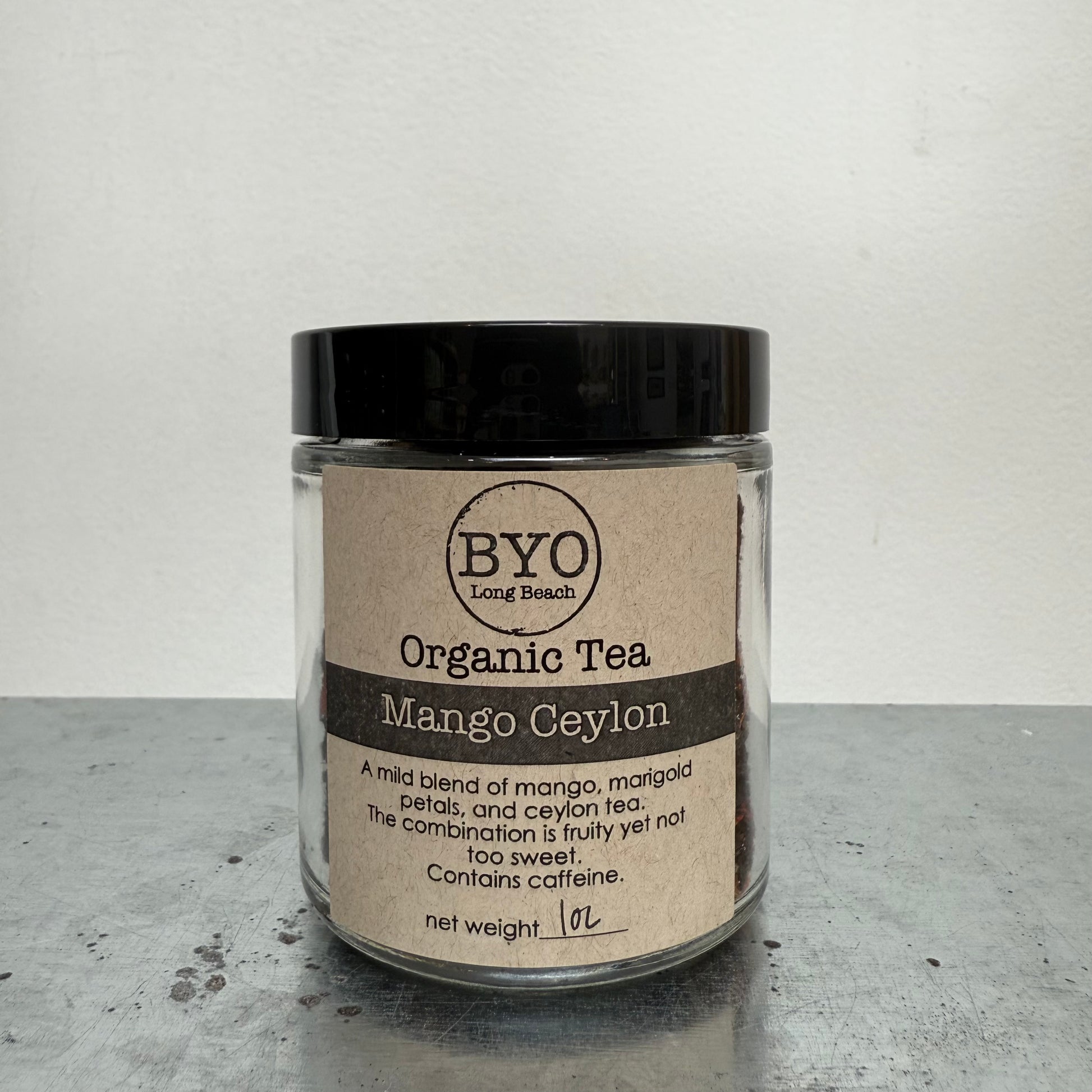 Glass jar of Organic Tea Mango Ceylon with a black lid on a gray surface.
