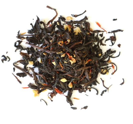 Dry black tea leaves with orange bits on a white background