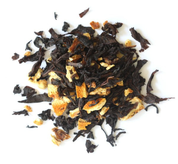 Dry black tea leaves with orange pieces on a white background