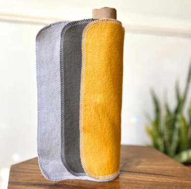 Three fabrics in gray, yellow, and light gray on a wooden surface with a blurred plant in the background.