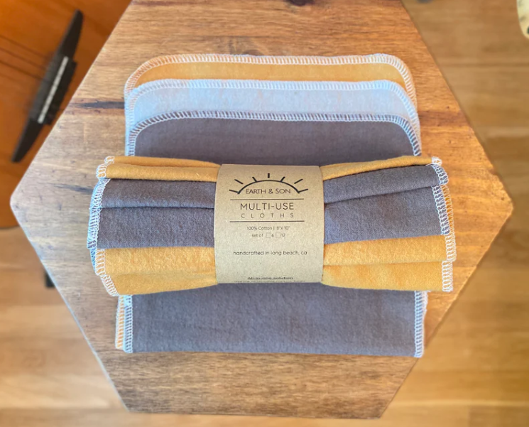 Set of multi-use cloths in gray and yellow on a wooden surface with a brand label.