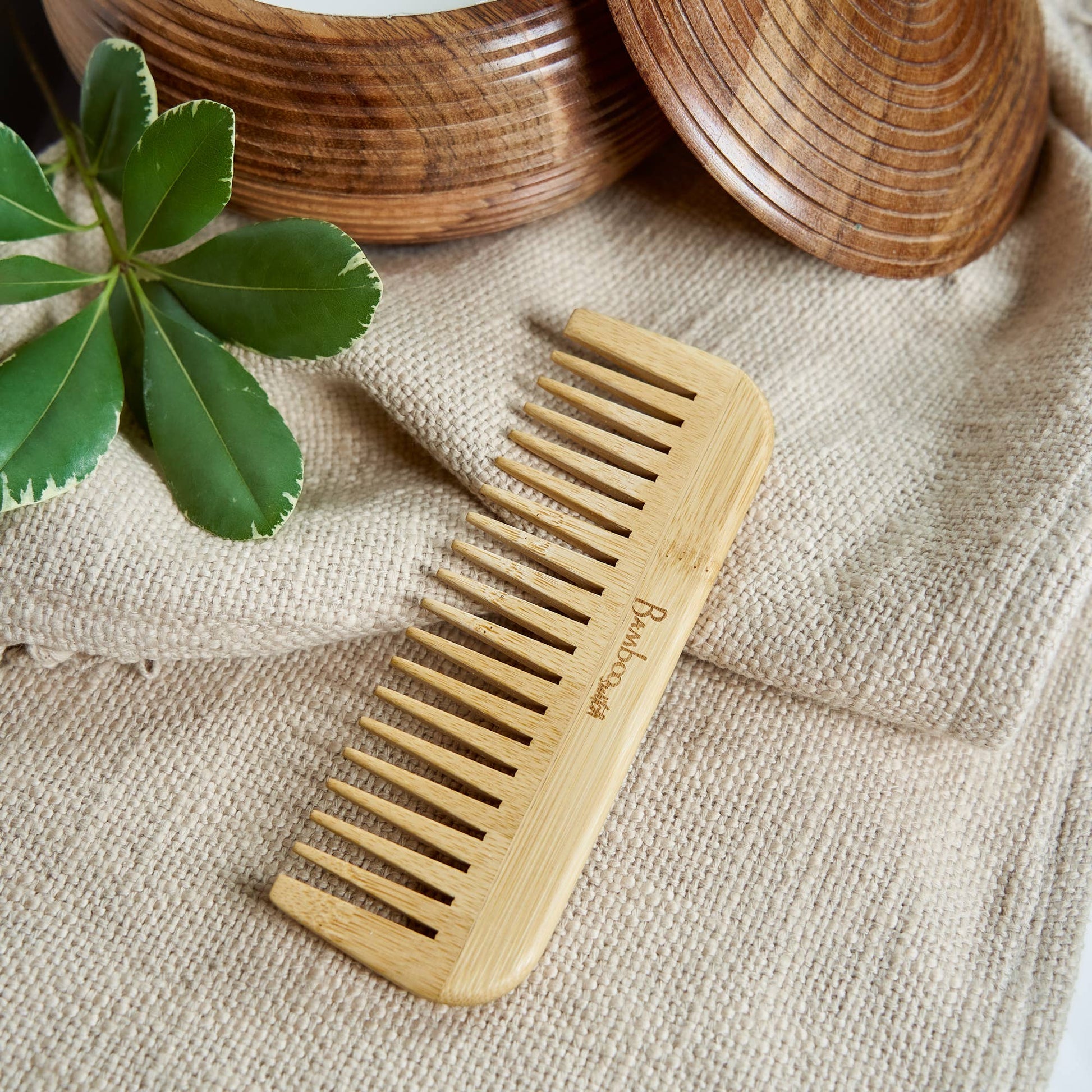 Wooden comb on a textured fabric surface with green leaves