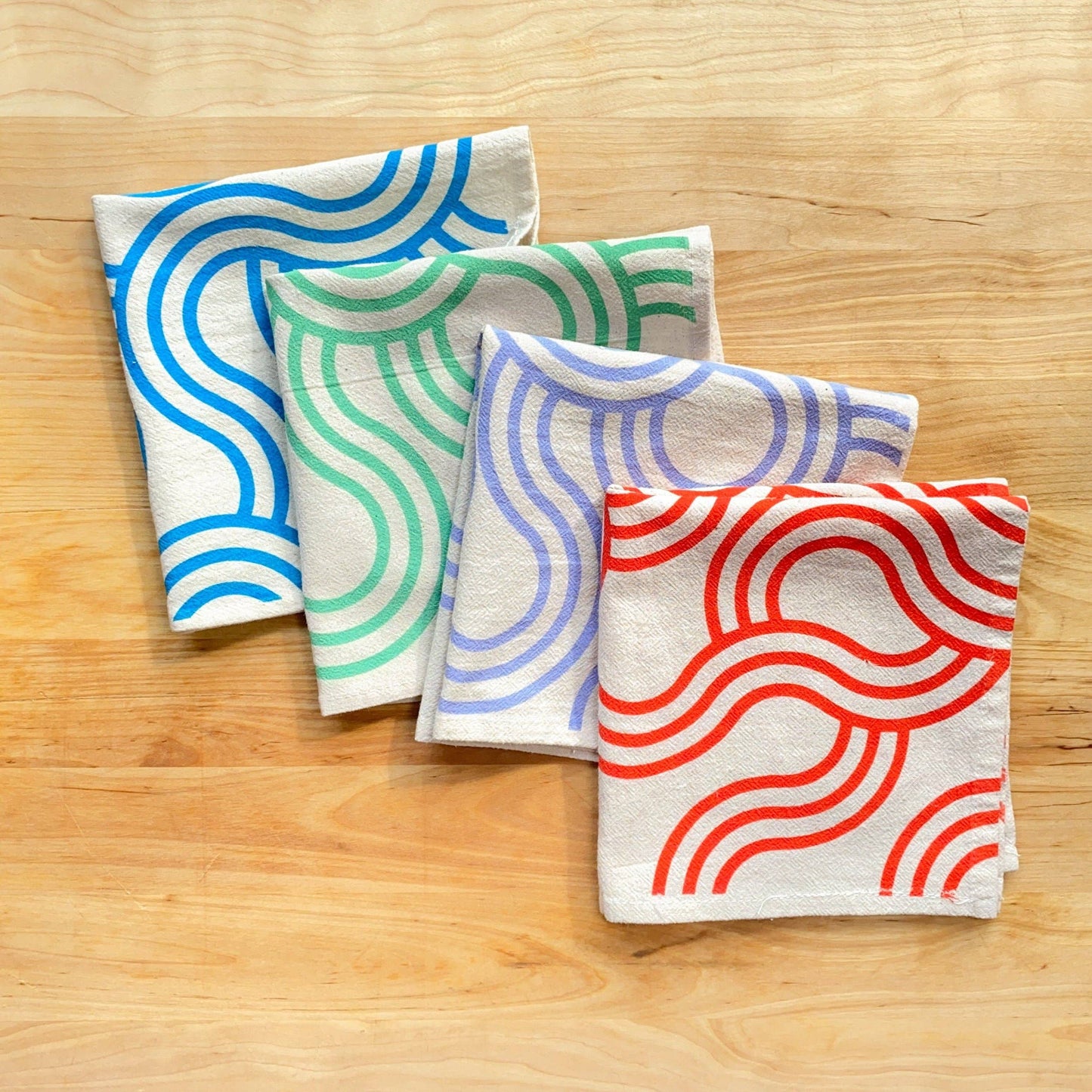 Four fabric towels with colorful wave patterns on a wooden surface