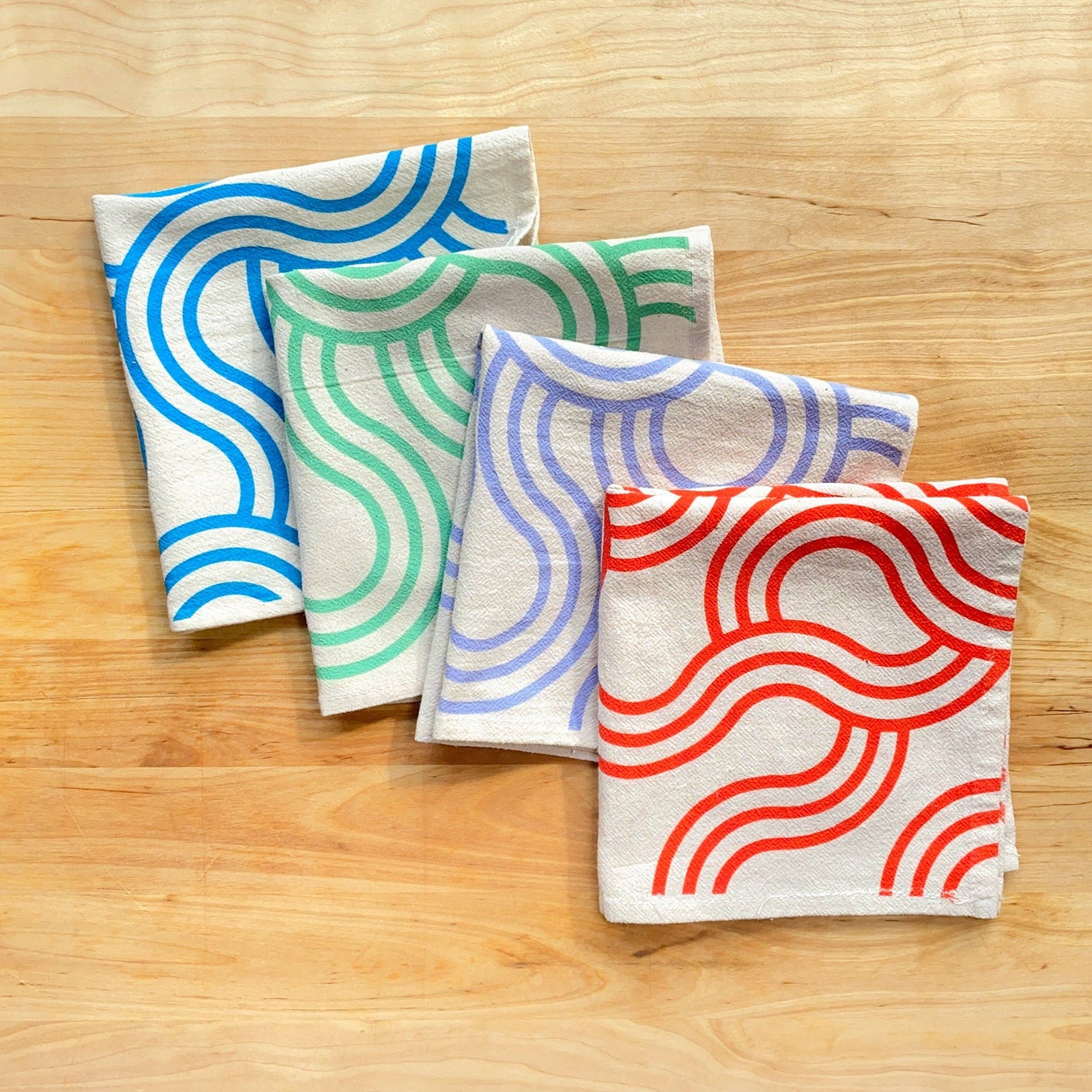 Four fabric towels with colorful wave patterns on a wooden surface