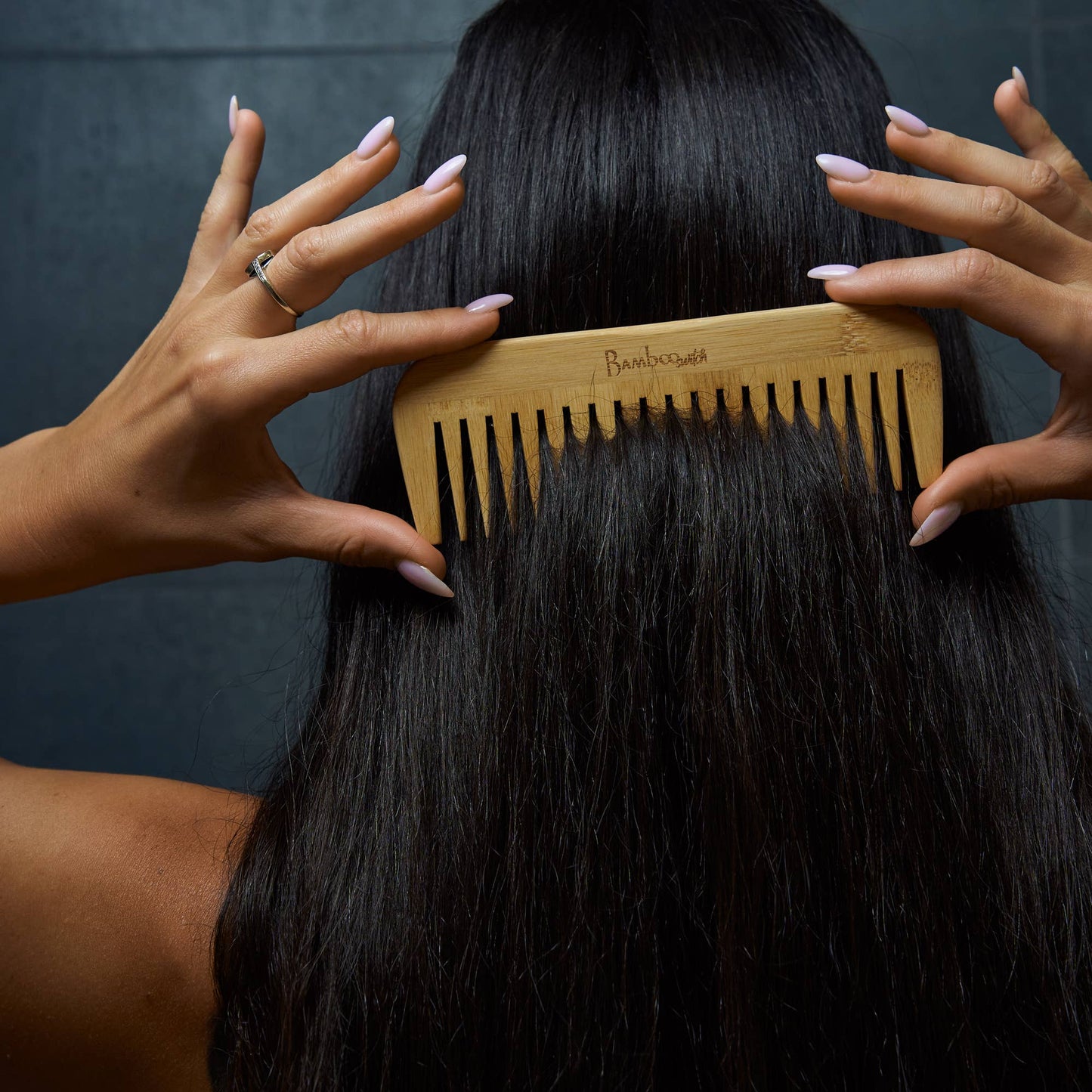 Person combing their hair with a wooden comb against a dark background