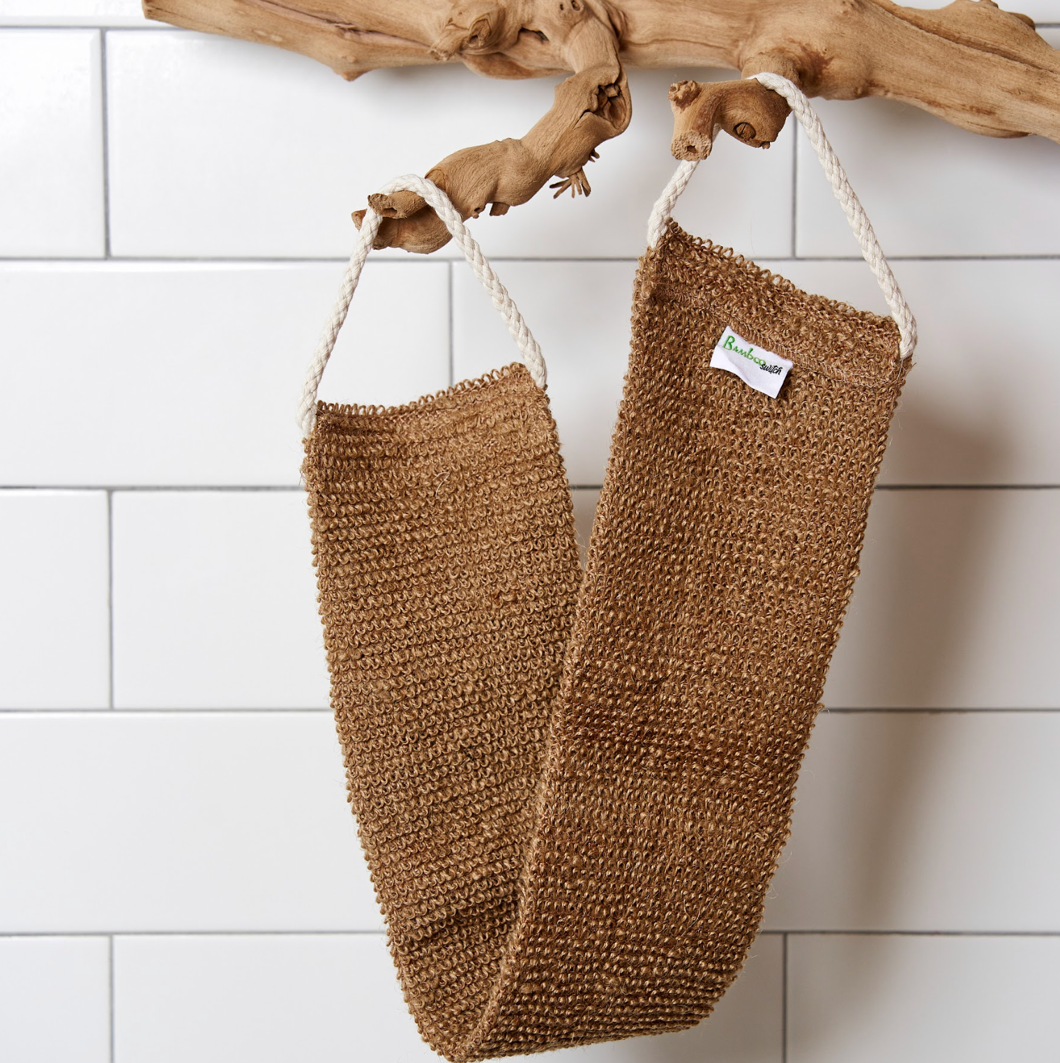 Two brown scrubbing brushes hanging on a white tiled wall with a piece of driftwood.