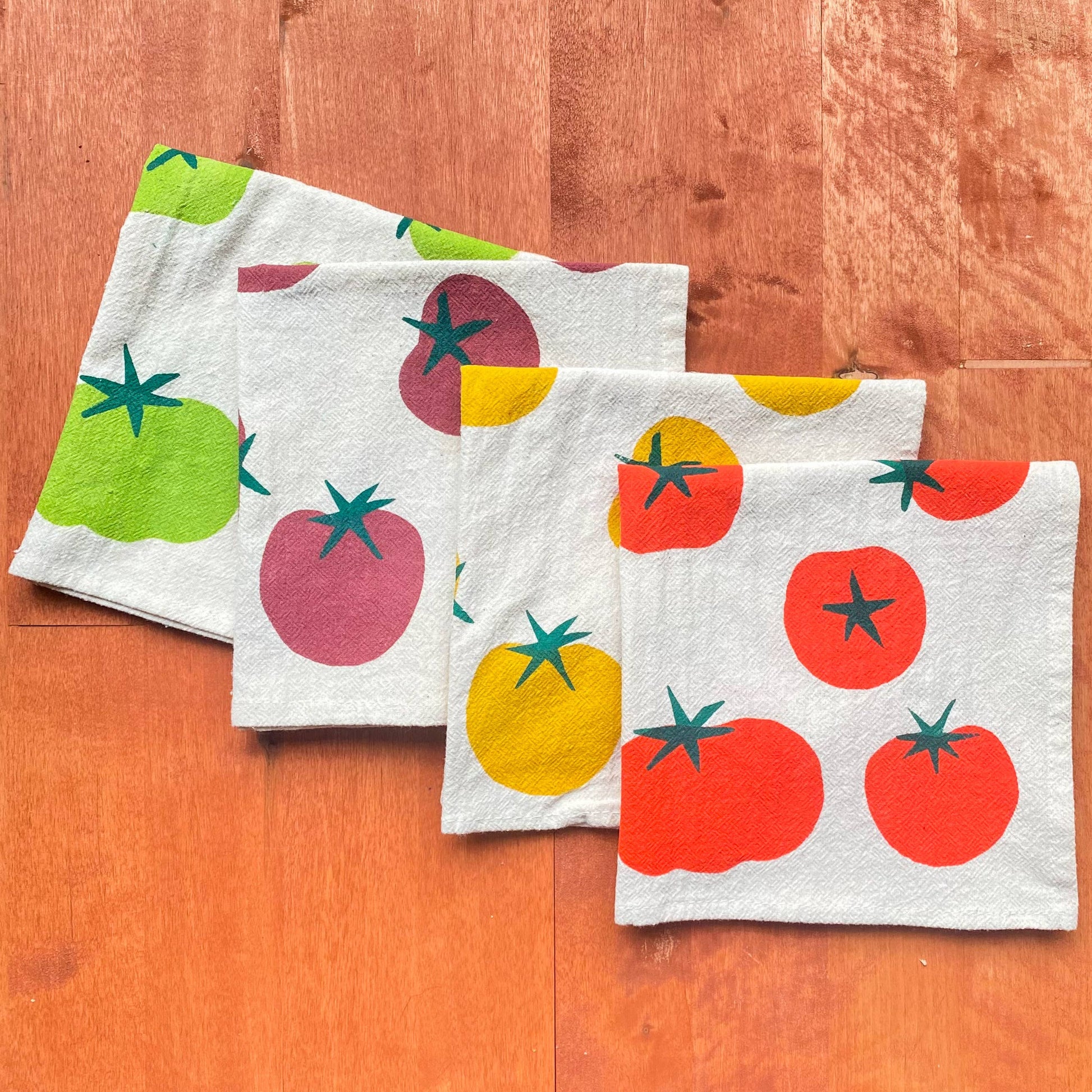 Set of four kitchen towels with tomato pattern on a wooden surface