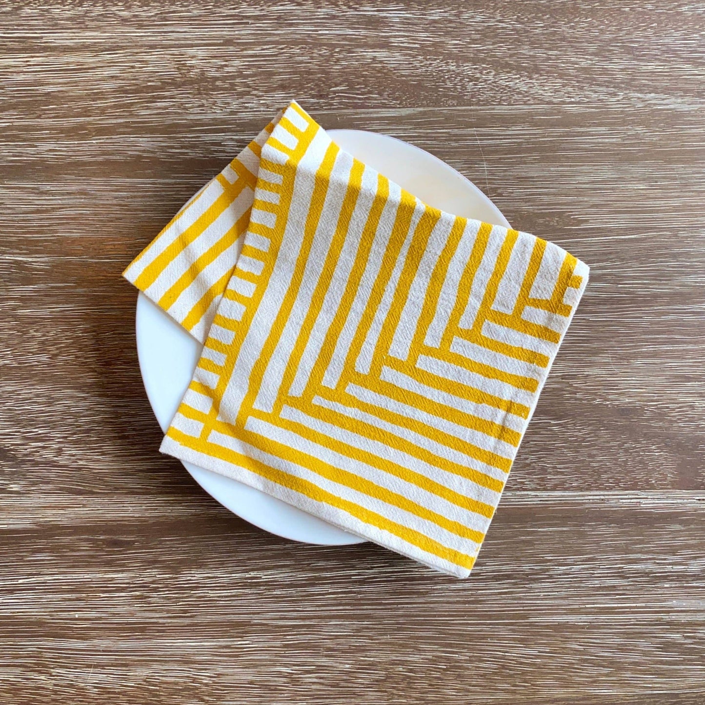 Yellow and white striped napkin on a white plate on a wooden surface