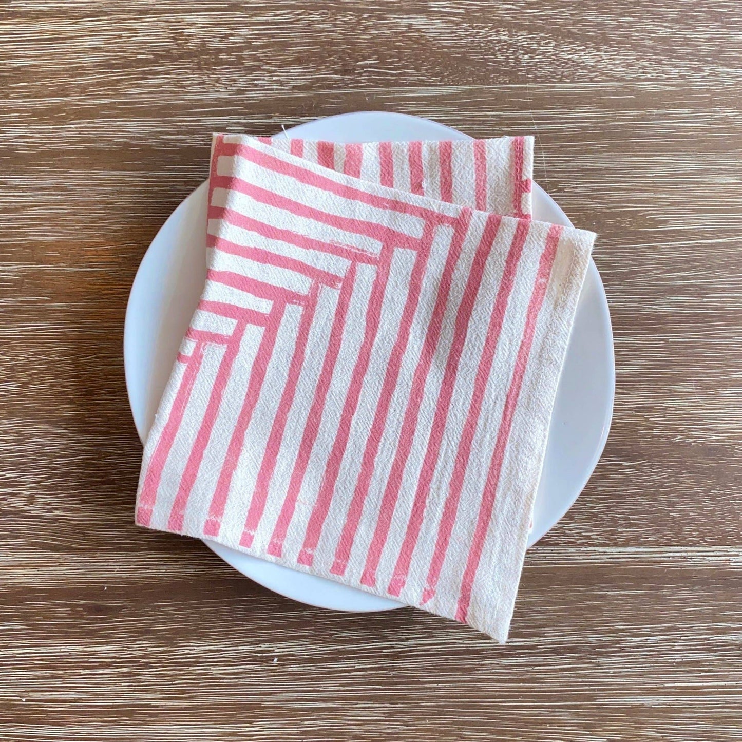 Folded pink and white striped napkin on a white plate with a wooden background