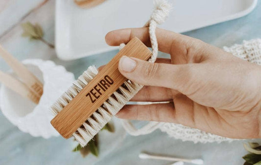 Hand holding a wooden brush with 'Zefiro' branding against a blurred background