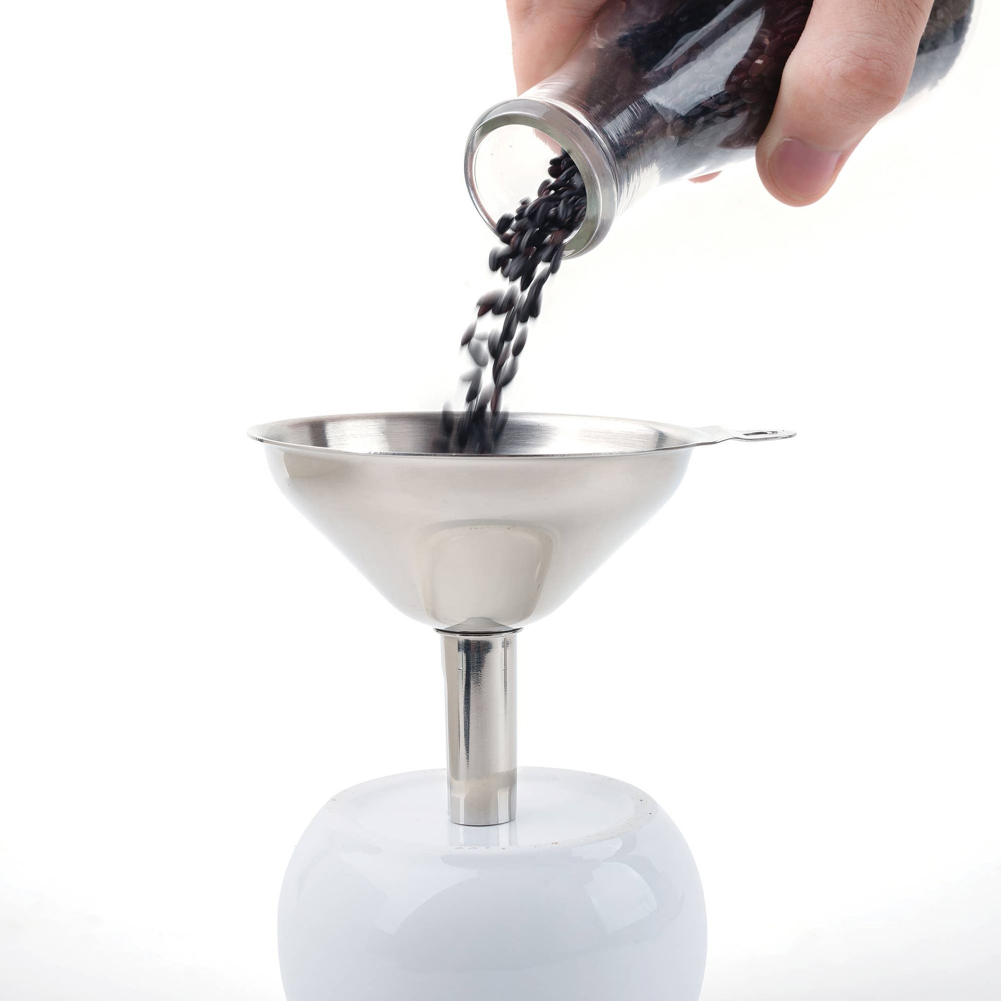 Hand pouring black coffee beans into a metal funnel on a white background