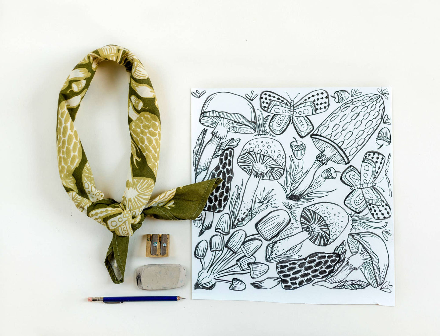 Green patterned scarf, coloring book with mushroom design, and coloring supplies on a white background