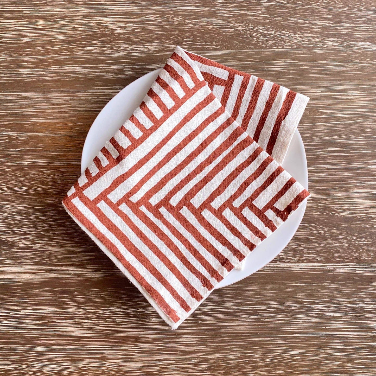 Folded red and white striped towel on a white plate against a wooden background
