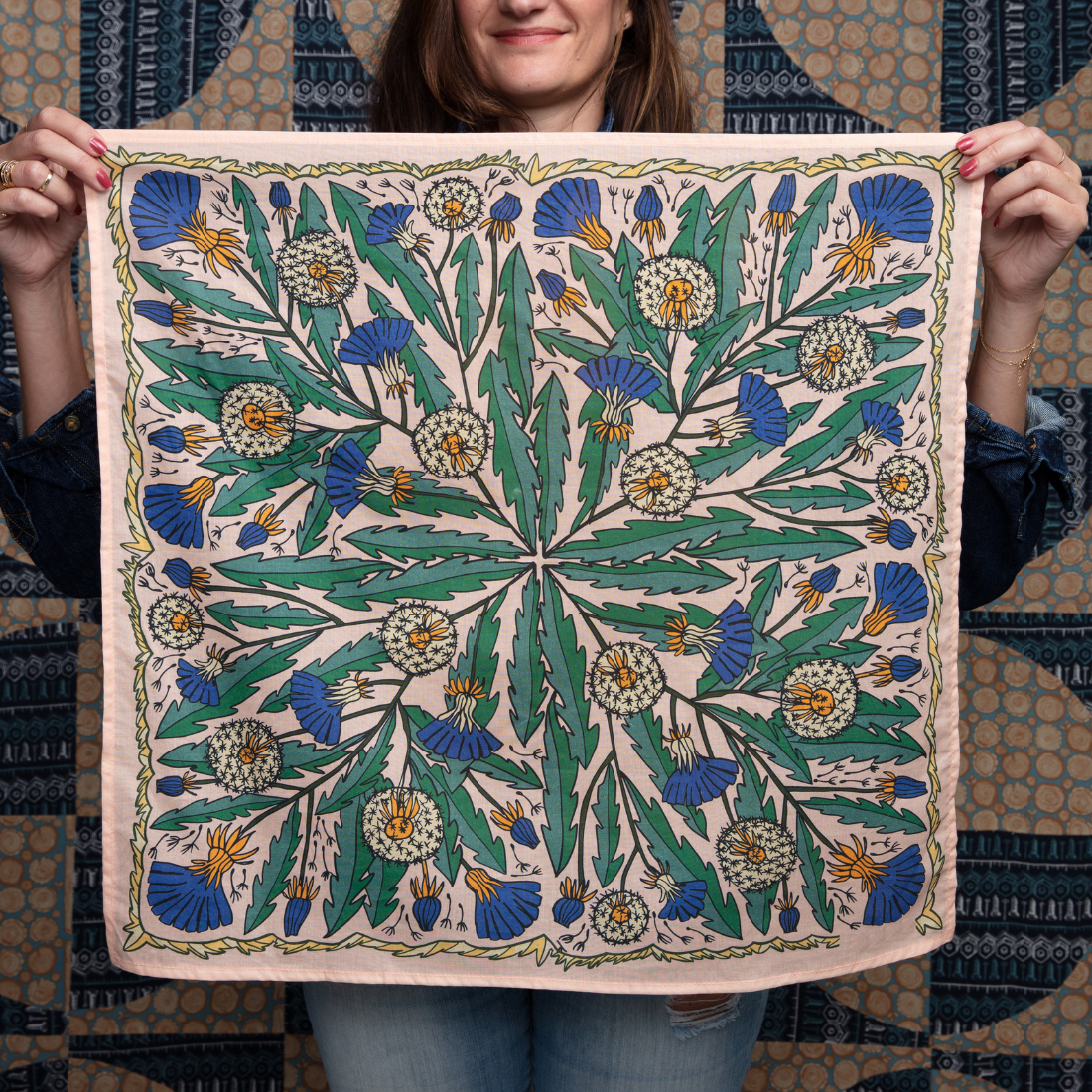 Person holding a decorative fabric with intricate green and blue floral pattern