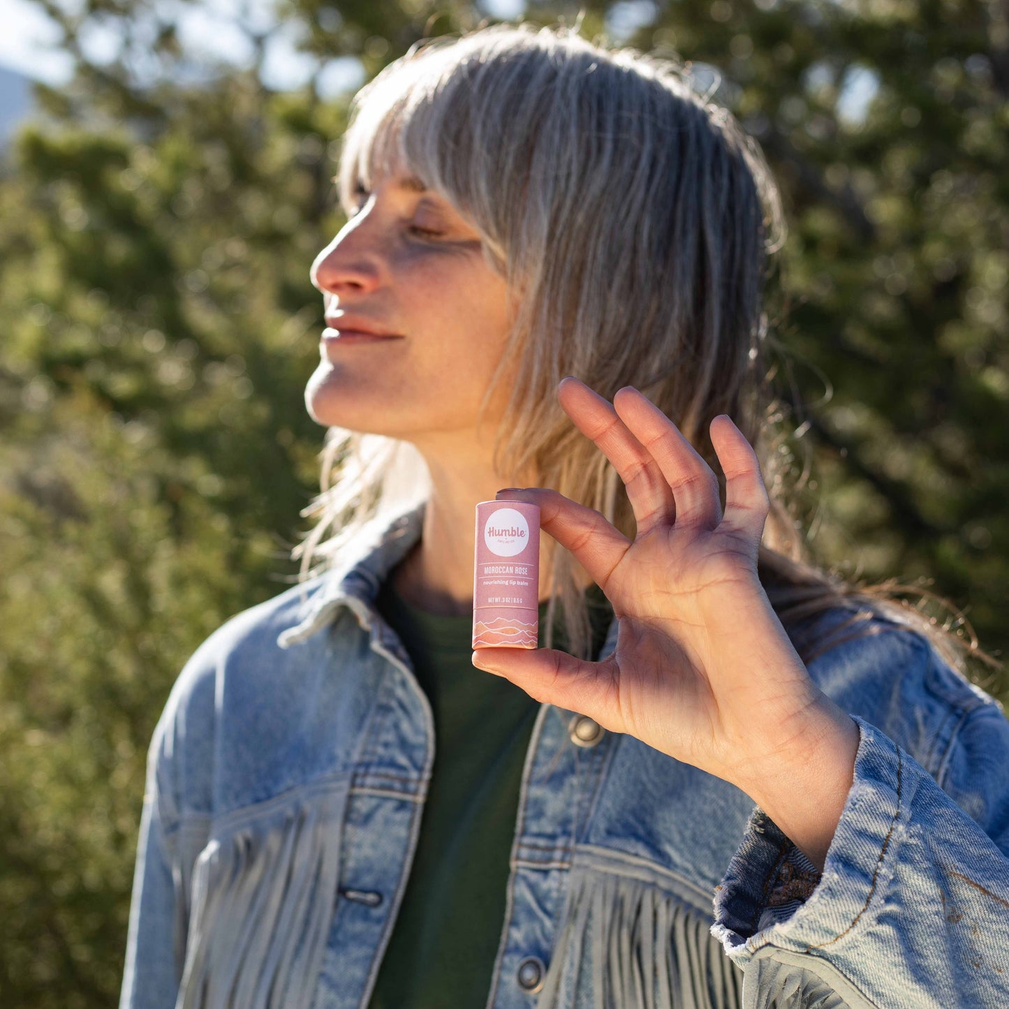 Person holding a pink bottle outdoors with trees in the background
