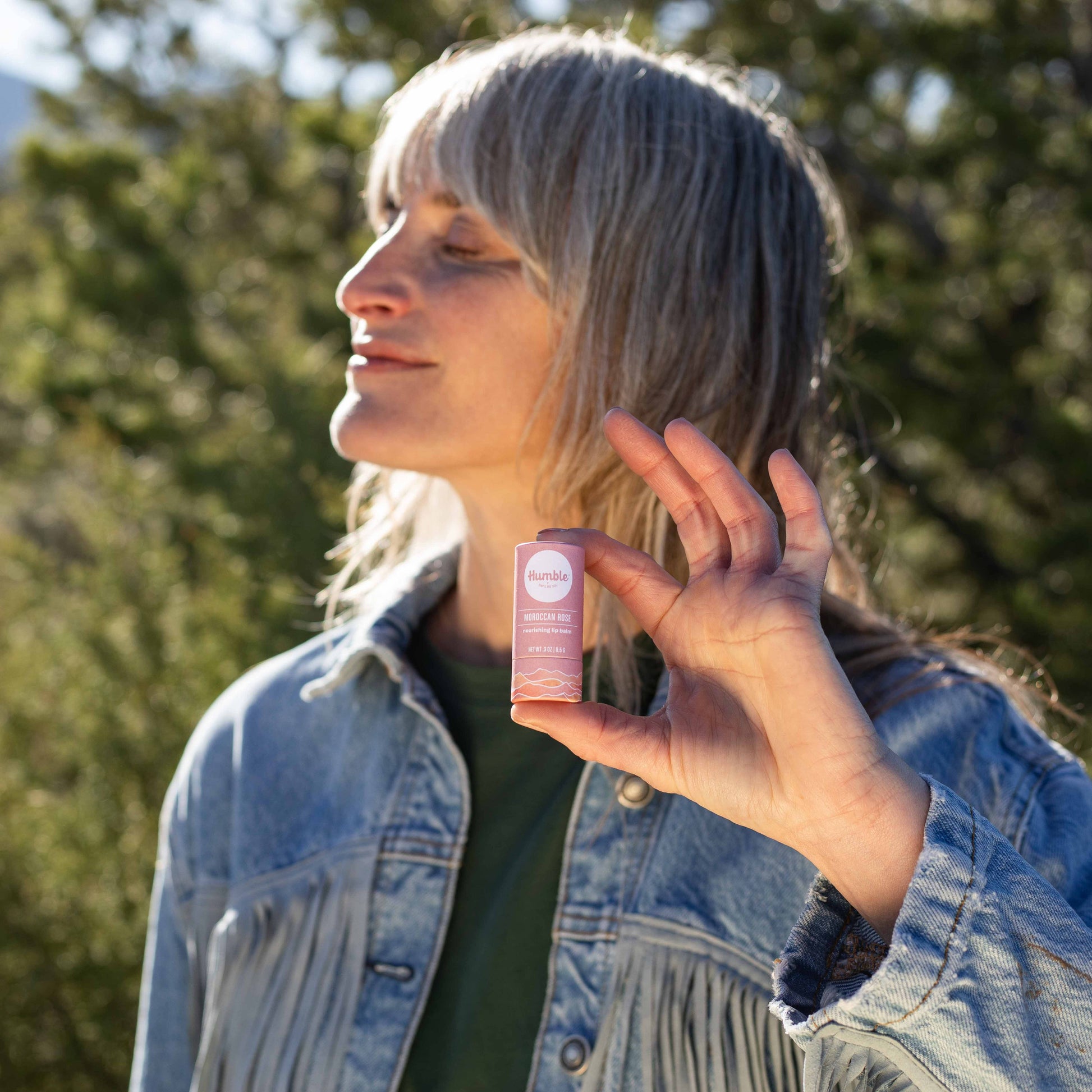 Person holding a pink bottle outdoors with trees in the background