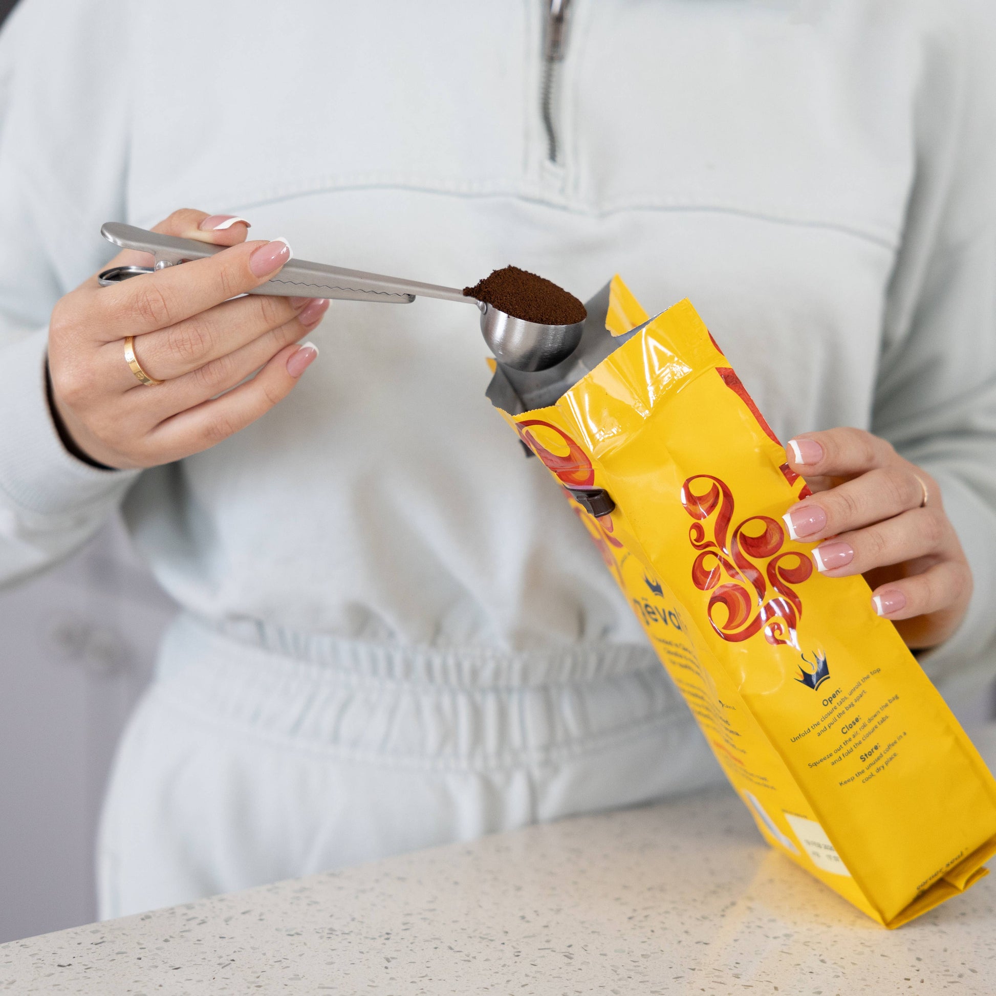 Person measuring coffee from a yellow package using a spoon.