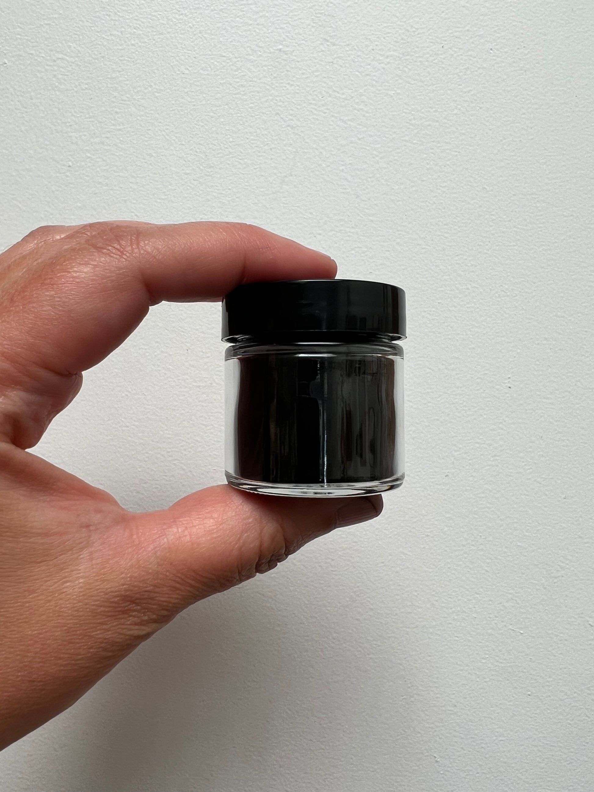 One ounce glass jar with black plastic lid containing charcoal powder