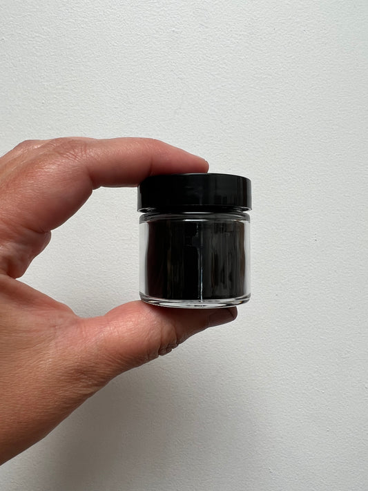 One ounce glass jar with black plastic lid containing charcoal powder