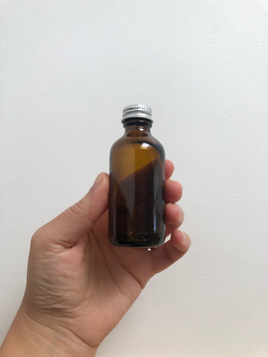 Hand holding a brown glass bottle with a silver cap against a white background