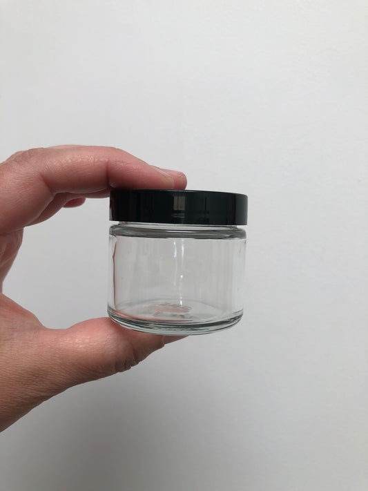 hand holding 2 ounce clear glass jar with black lid