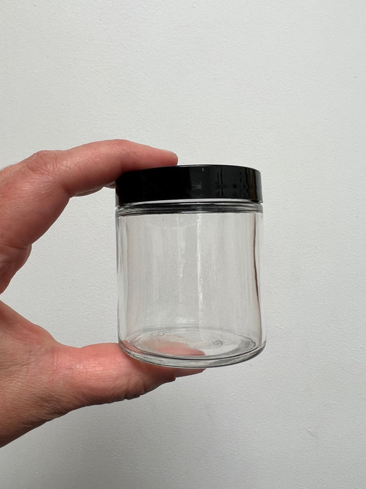 hand holding 4 ounce clear glass jar with black lid