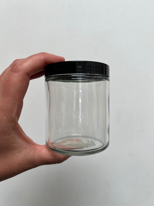 hand holding a clear glass jar with a black lid