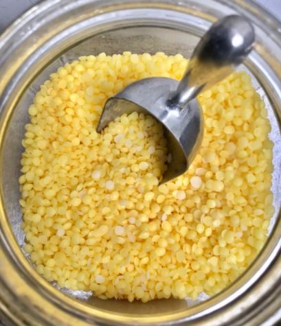 Jar of beeswax pellets with metal scoop