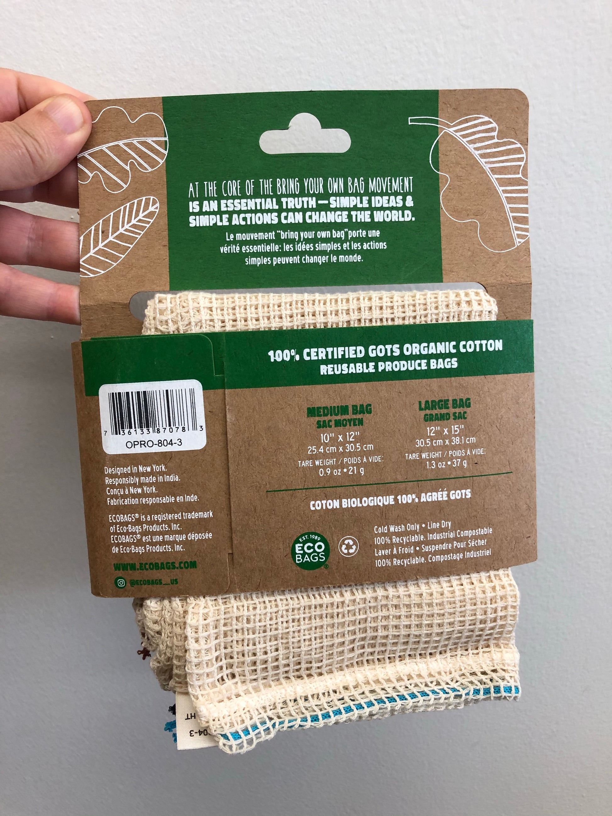 Cardboard packaging holding a set of 3 cotton mesh produce bags, all medium size. Bags are natural color with an open weave. Image shows back side of packaging.